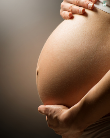 Close-up of a pregnant belly held gently by hands.