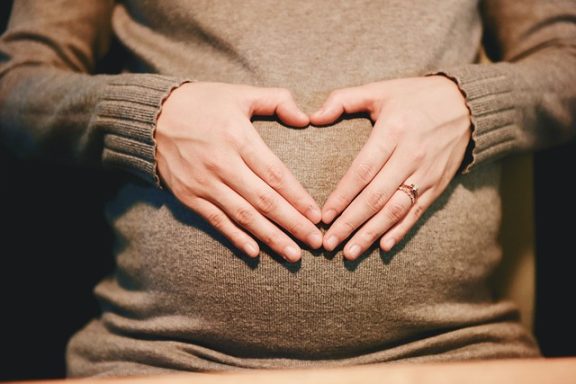 Hands forming a heart shape over a pregnant belly.